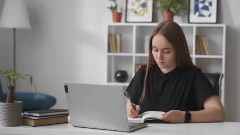 young-woman-is-reading-information-on-screen-of-laptop-and-writing-in-notebook-learning-in-home-distant-education-online-course-for-professional-development
